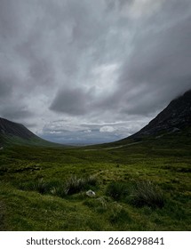 Dramatic cloudy sky over the lush green valley of Glencoe, Scotland. Moody landscape with rolling hills and misty mountains.