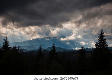 Dramatic cloudy sky over a mountain landscape with pine trees.