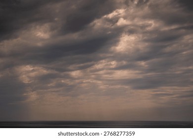 Dramatic cloudy sky over ocean horizon at sunset. Dark storm cloud with warm light breaking through. Moody seascape with vast sky and calm sea below