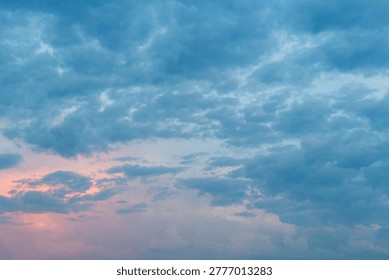 Dramatic cloudy sky with pink orange sunset glow breaking through gray blue clouds.
