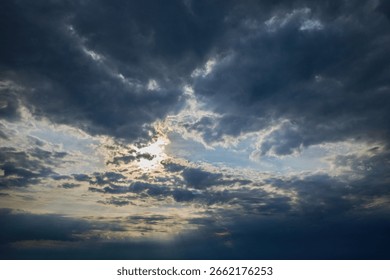 Dramatic cloudy sky with sun rays shining through dark storm clouds over the horizon.