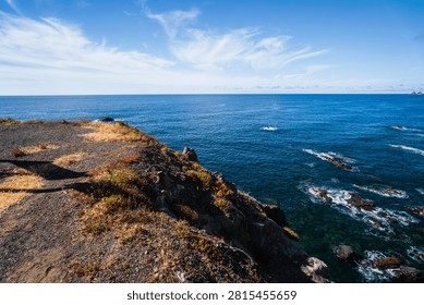 Dramatic coastal cliffs covered in sparse vegetation overlook the vast, deep blue waters of the Atlantic Ocean with rocky outcrops
