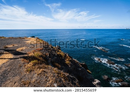 Dramatic coastal cliffs covered in sparse vegetation overlook the vast, deep blue waters of the Atlantic Ocean with rocky outcrops