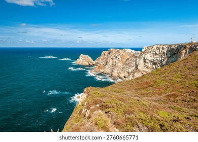 Dramatic coastal cliffs with lighthouse overlooking deep blue Atlantic ocean, rugged rocks and wild vegetation, northern Spain coastline landscape photography