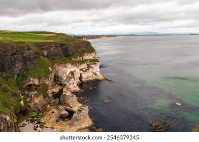 Dramatic coastal cliffs with lush green grass, white rock formations, and calm ocean waters under a cloudy sky. A stunning natural landscape by the sea. - Powered by Shutterstock