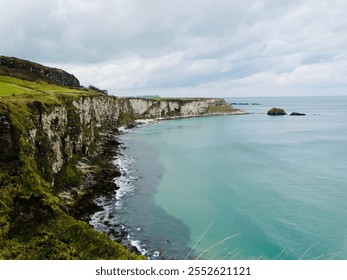 Dramatic coastal cliffs in Northern Ireland with lush green grass, turquoise waters, and a cloudy sky, showcasing the rugged beauty of the Irish coastline and its breathtaking natural scenery - Powered by Shutterstock