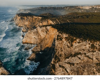 Dramatic coastal cliffs with ocean waves crashing below, aerial view of rugged shoreline landscape with green hills and rocky formations under soft light. Portugal