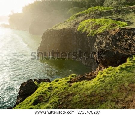 Dramatic coastal cliffs plunge into turquoise ocean in Mauritius, showcasing nature’s artistry. Eroded rock formations meet vibrant greenery bathed in golden hour light; sunbeams illuminate the powerful landscape.