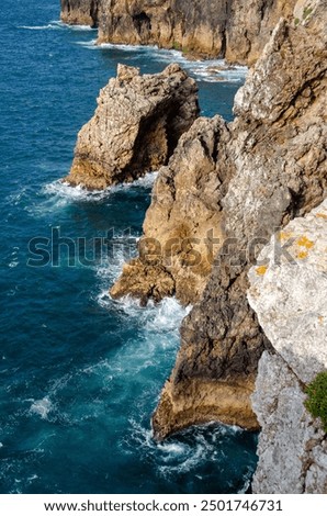 Dramatic coastal cliffs with rugged rocks jutting into the vibrant blue ocean. Waves crash against the cliffs, showcasing the raw beauty and power of nature. Perfect for coastal and nature themes.