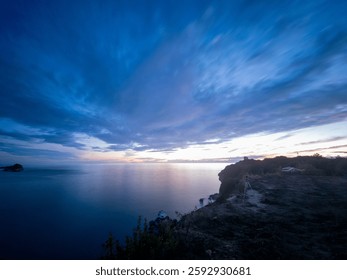 A dramatic coastal landscape with twilight clouds over the tranquil ocean, captured from a high cliff.