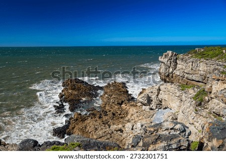 Dramatic coastal landscape where rugged mountains meet the deep blue ocean under a clear sky. A scenic shoreline with rocky cliffs, turquoise water, and lush coastal vegetation creates a powerful contrast between land and sea, ideal for travel, nature, and adventure concepts.