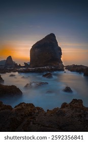 Dramatic coastal rock formations at sunset with smooth water and vibrant sky, creating a serene seascape scene.