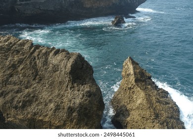 A dramatic coastal scene featuring waves crashing against a rocky shore. The force of the water is accentuated by the surrounding lush green algae