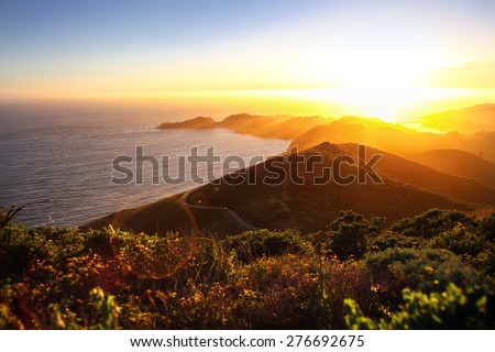 Dramatic coastal sunset with island peninsula and golden light ocean