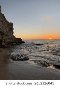 Dramatic coastal sunset with rocky cliffs and waves on secluded beach