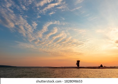 Dramatic Colorful Orange To Blue Sunset Or Sunrise Sky Landscape With Lake Or River Bank And Tree Silhouette. Natural Beautiful Cloudscape Dawn Wallpaper.Ripple Water Reflection Twilight Panorama