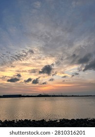Dramatic colorful sunset sky over calm coastal waters with silhouettes and industrial harbor
