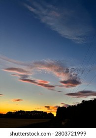 Dramatic colourful sunset with silhouetted trees and clouds over rural field at dusk