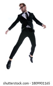 dramatic cool young man in black suit jumping in the air, looking to side on white background, full body
