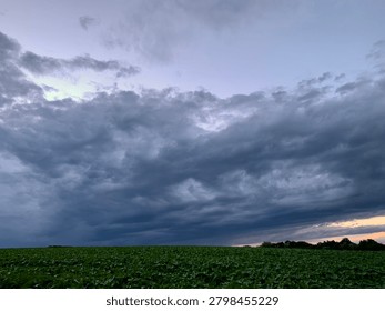Dramatic crepuscular rays shining through dark storm clouds at sunset. Sunlight streams from behind the cloud cover, illuminating the sky above a silhouette of trees and creating a striking atmospheric landscape.
