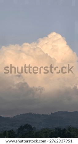 A dramatic cumulus cloud formation billows across a hazy sky, with a distant treeline silhouetted against the horizon