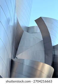 Dramatic curved metallic panels create flowing sculptural forms with sharp angular shadows against clear blue sky, showcasing bold contemporary architecture