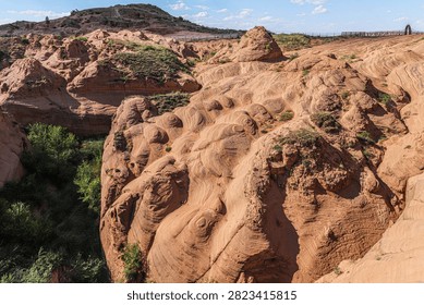 Dramatic Danxia landform featuring distinctive wave-patterned red sandstone formations in Jingbian area, showcasing natural geological sculptural beauty and scenic valley landscape.
