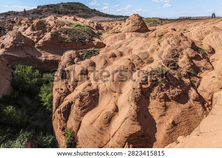 Dramatic Danxia landform featuring distinctive wave-patterned red sandstone formations in Jingbian area, showcasing natural geological sculptural beauty and scenic valley landscape.