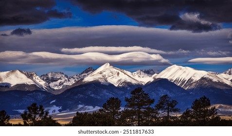 Dramatic dark clouds, and lenticular clouds over the snow covered Colorado Rocky Mountains and valley below on a cold winter evening 