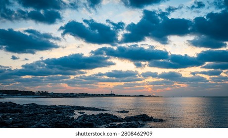 Dramatic dark clouds over a calm ocean and rocky volcanic coastline during a beautiful colorful sunset.