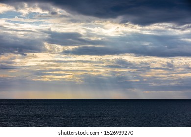 Dramatic dark cloudy sky and sun shining over over sea, stormy weather, rays of sun
