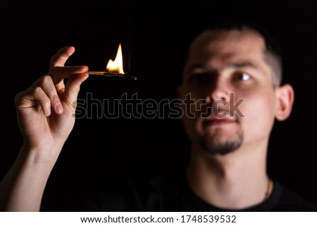 Dramatic dark portrait of man and lit match fire over black background