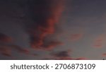 Dramatic, dark sky at twilight featuring wispy, elongated clouds painted in deep shades of pink and red. Captures a moody, abstract, and vibrant sunset or sunrise cloudscape.