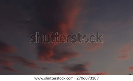 Dramatic, dark sky at twilight featuring wispy, elongated clouds painted in deep shades of pink and red. Captures a moody, abstract, and vibrant sunset or sunrise cloudscape.