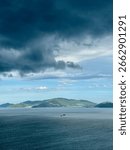 Dramatic dark storm clouds gathering over the ocean with a distant green island on the horizon. Moody and atmospheric seascape view.