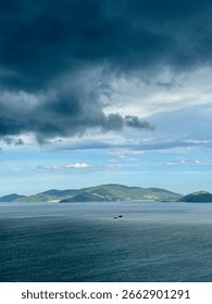Dramatic dark storm clouds gathering over the ocean with a distant green island on the horizon. Moody and atmospheric seascape view.