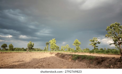 Dramatic dark storm clouds gathering over an empty agricultural dirt field and trees, beautiful impending rain in the rural countryside.