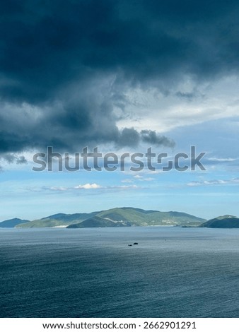 Dramatic dark storm clouds gathering over the ocean with a distant green island on the horizon. Moody and atmospheric seascape view.