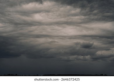 Dramatic dark storm clouds rolling across the sky above a forested horizon, creating a moody and powerful atmosphere. Copy space.