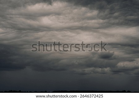 Dramatic dark storm clouds rolling across the sky above a forested horizon, creating a moody and powerful atmosphere. Copy space.