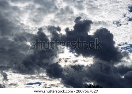 Dramatic dark storm clouds swirling in the sky with a bright light breaking through, capturing a moody atmosphere and the powerful contrast of a brewing summer tempest