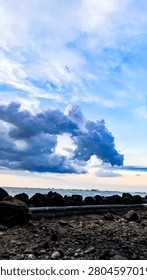Dramatic dark storm clouds with a unique circular hole formation over a rocky coastline and calm sea during sunset.