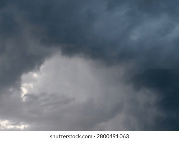 A dramatic dark stormy sky with a powerful vortex of storm clouds spinning. A single majestic sunbeam pierces through the heavy dense overcast, creating a stark high contrast between light and deep shadow in the atmosphere.