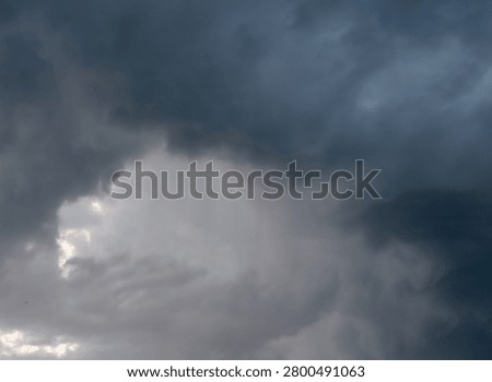 A dramatic dark stormy sky with a powerful vortex of storm clouds spinning. A single majestic sunbeam pierces through the heavy dense overcast, creating a stark high contrast between light and deep shadow in the atmosphere.