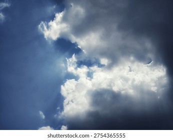 Dramatic dark and white clouds with sunlight breaking through a blue sky, creating powerful light rays and a dynamic cloudscape. Perfect for weather, nature background, sky atmosphere, and dramatic sky concepts.