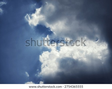 Dramatic dark and white clouds with sunlight breaking through a blue sky, creating powerful light rays and a dynamic cloudscape. Perfect for weather, nature background, sky atmosphere, and dramatic sky concepts.