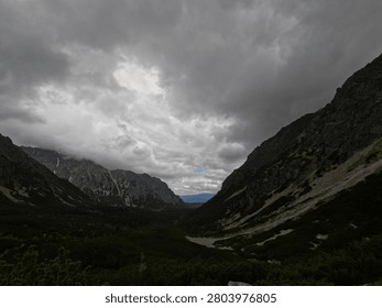 Dramatic deep alpine mountain valley with steep rocky slopes, scree, snow patches and heavy fog covering the peaks in the High Tatras.