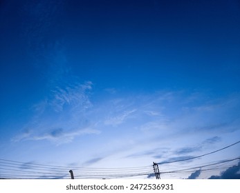 Dramatic deep blue sunset sky with clouds and silhouetted electric wires.