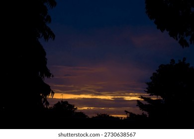 Dramatic deep purple twilight sky with a narrow golden horizon streak framed by dark tree silhouettes.