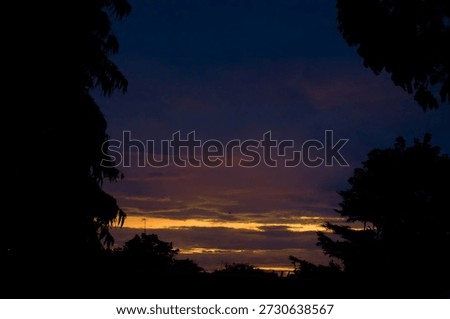 Dramatic deep purple twilight sky with a narrow golden horizon streak framed by dark tree silhouettes.